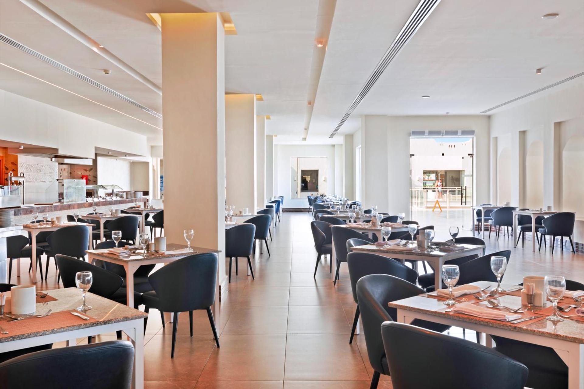 فندق رويال جراند شرم ريزورت شرم الشيخ المظهر الخارجي الصورة The photo shows the interior of a modern restaurant. The space is bright and airy, featuring large windows that allow natural light to flood in. There are several tables arranged throughout the room, each covered with placemats and set with glasses a