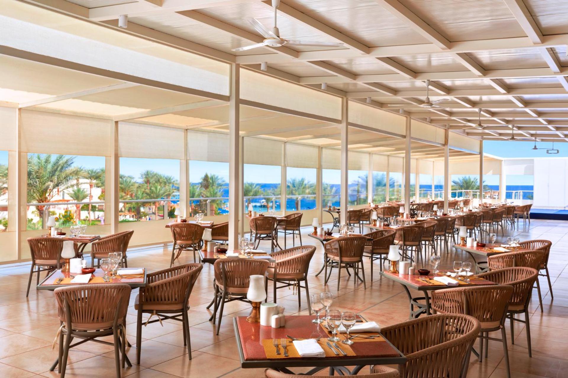 فندق رويال جراند شرم ريزورت شرم الشيخ المظهر الخارجي الصورة The photo shows a spacious dining area in a restaurant with a modern and airy design. It features numerous wooden tables set with glasses and cutlery, arranged in a way that gives an open feel. Large windows provide a view of the outside, showcasing 