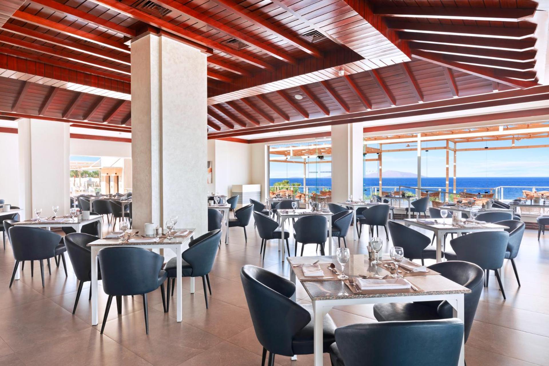 فندق رويال جراند شرم ريزورت شرم الشيخ المظهر الخارجي الصورة The photo shows a modern restaurant interior with a spacious and well-lit design. There are several tables set for dining, featuring white tablecloths and elegant dinnerware. The chairs are sleek and dark, contrasting with the bright surroundings. La