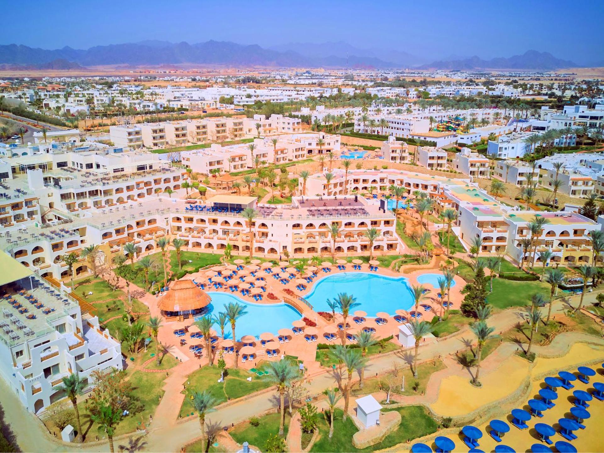 فندق رويال جراند شرم ريزورت شرم الشيخ المظهر الخارجي الصورة The photo shows an aerial view of a resort complex. There are several buildings arranged around a central area that features swimming pools. The pools are surrounded by palm trees and lounge chairs, indicating a tropical or sunny climate. In the back