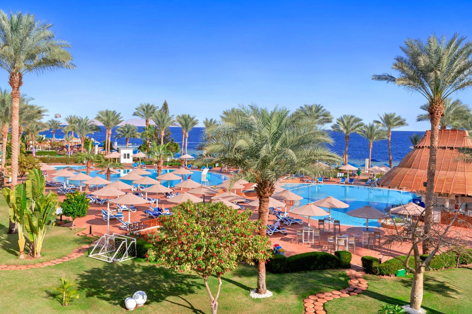 فندق رويال جراند شرم ريزورت شرم الشيخ المظهر الخارجي الصورة The photo depicts a tropical resort setting by the sea. It features a large swimming pool surrounded by sun loungers and umbrellas. Lush palm trees are scattered throughout the area, providing shade and a picturesque backdrop. In the background, you 