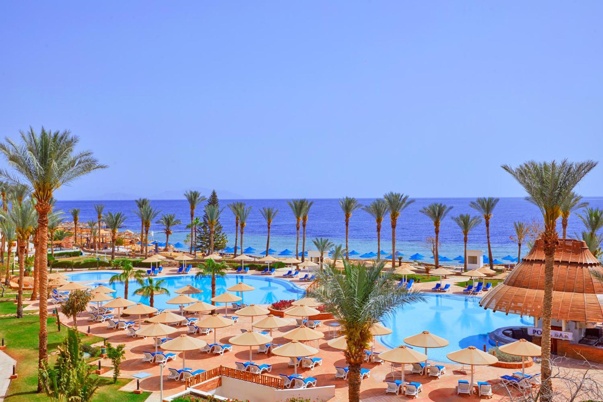 فندق رويال جراند شرم ريزورت شرم الشيخ المظهر الخارجي الصورة The photo showcases a beautiful resort setting by the sea. It features a large swimming pool surrounded by sunny lounge chairs and umbrellas, perfect for relaxation. The area is adorned with lush palm trees, adding to the tropical vibe. In the backgr