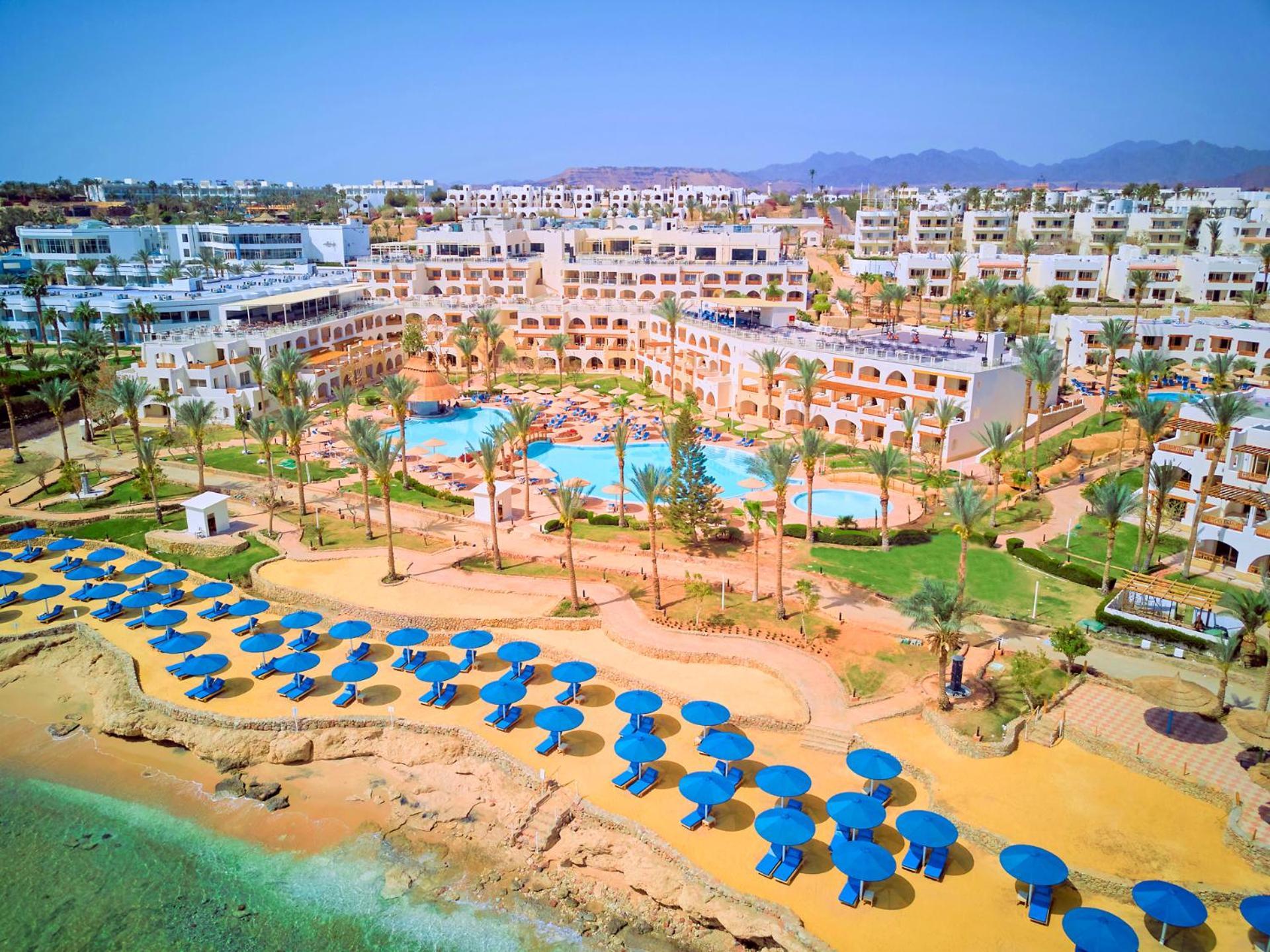 فندق رويال جراند شرم ريزورت شرم الشيخ المظهر الخارجي الصورة The photo shows a vibrant resort area with several buildings that appear to be accommodations or hotel units. There are multiple swimming pools surrounded by palm trees, creating a tropical atmosphere. In the foreground, there is a beach area with sa