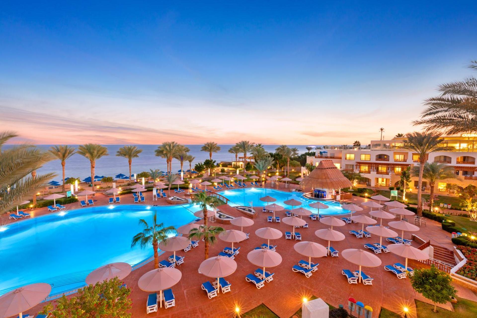 فندق رويال جراند شرم ريزورت شرم الشيخ المظهر الخارجي الصورة The photo showcases a luxurious resort setting with two large swimming pools, surrounded by lounge chairs and umbrellas. Palm trees are interspersed around the pool area, enhancing the tropical feel. In the background, there’s a view of the ocean, an