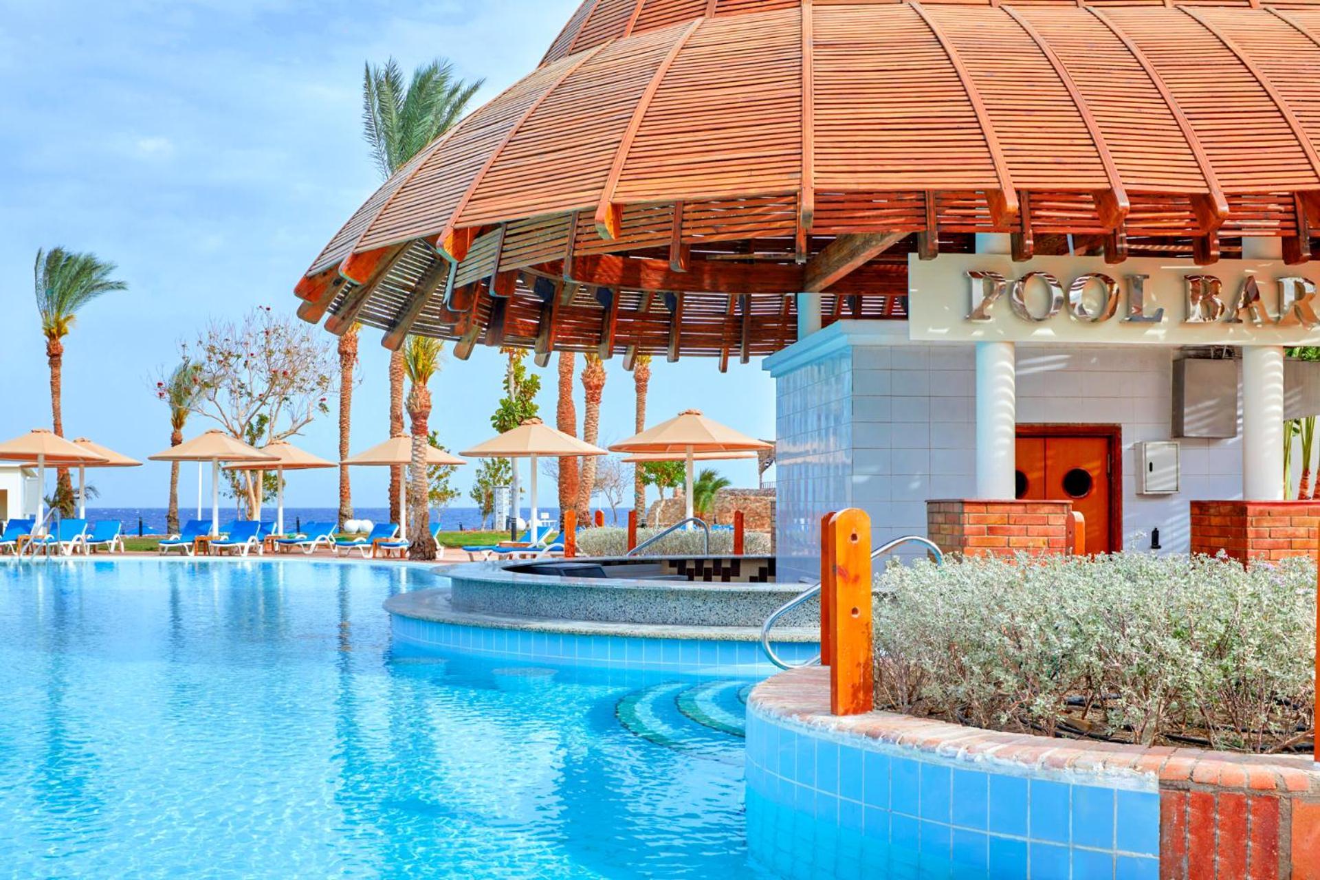 فندق رويال جراند شرم ريزورت شرم الشيخ المظهر الخارجي الصورة The photo depicts a picturesque pool area at a resort. In the foreground, there is a clear and inviting swimming pool with curved edges, surrounded by a light blue tile border. To the side, a pool bar is visible with a wooden roof and stylish archite